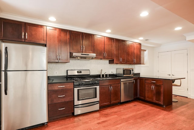 kitchen with a sink, under cabinet range hood, stainless steel appliances, dark countertops, and a peninsula