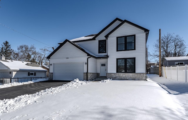 modern farmhouse featuring an attached garage, fence, aphalt driveway, and stone siding