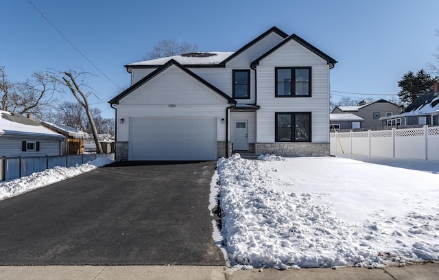 modern farmhouse with an attached garage, fence, aphalt driveway, and stone siding