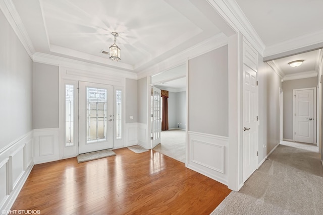 foyer featuring a tray ceiling, visible vents, a decorative wall, ornamental molding, and wood finished floors