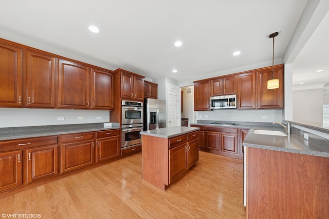 kitchen featuring appliances with stainless steel finishes, a center island, light wood-style floors, pendant lighting, and a sink