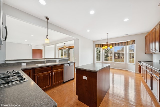 kitchen with dark countertops, stainless steel appliances, light wood-type flooring, pendant lighting, and a sink