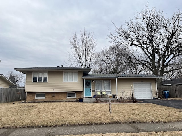 tri-level home featuring a garage, aphalt driveway, a front lawn, and fence