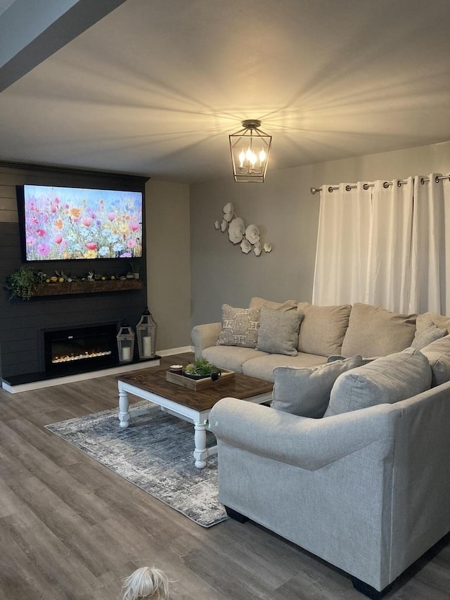 living room with a warm lit fireplace, a chandelier, and wood finished floors