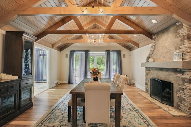 dining area with lofted ceiling with beams, light wood-style flooring, a fireplace, and a chandelier