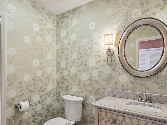 bathroom with vanity, toilet, and wallpapered walls