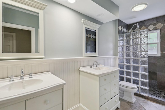 full bath with wainscoting, toilet, a sink, walk in shower, and two vanities