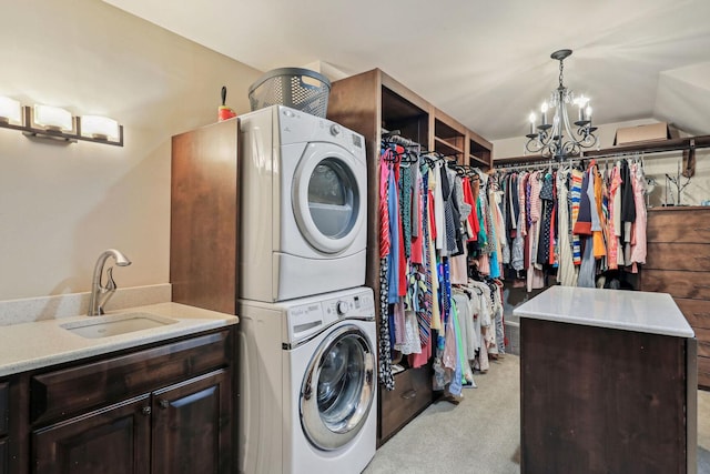 washroom featuring cabinet space, an inviting chandelier, light carpet, a sink, and stacked washing maching and dryer