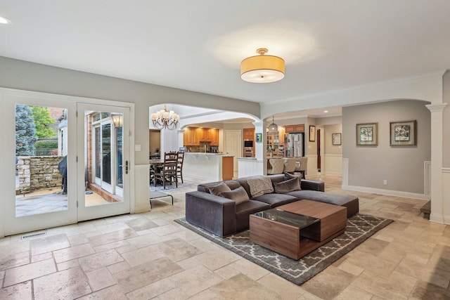 living room featuring arched walkways, stone tile flooring, visible vents, decorative columns, and an inviting chandelier