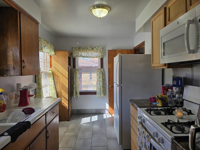 kitchen with white appliances, light tile patterned flooring, and brown cabinetry