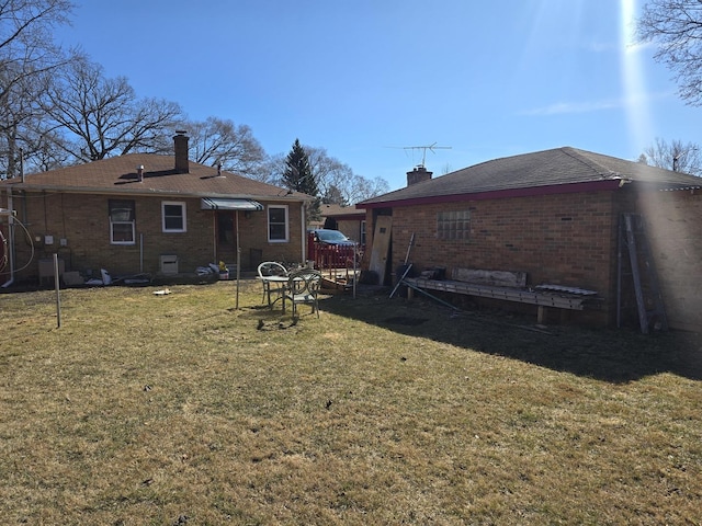 back of property featuring a yard, brick siding, and a chimney