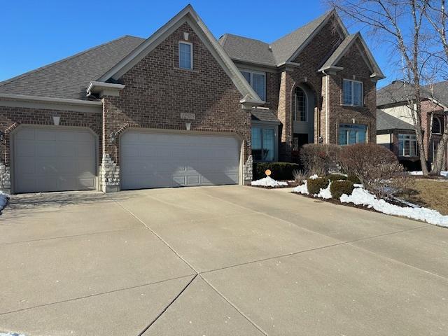 traditional home with roof with shingles, concrete driveway, and brick siding