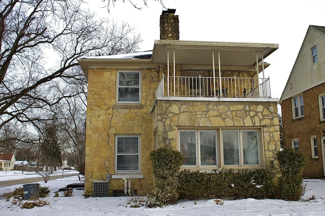 exterior space featuring a balcony, stone siding, central air condition unit, and a chimney