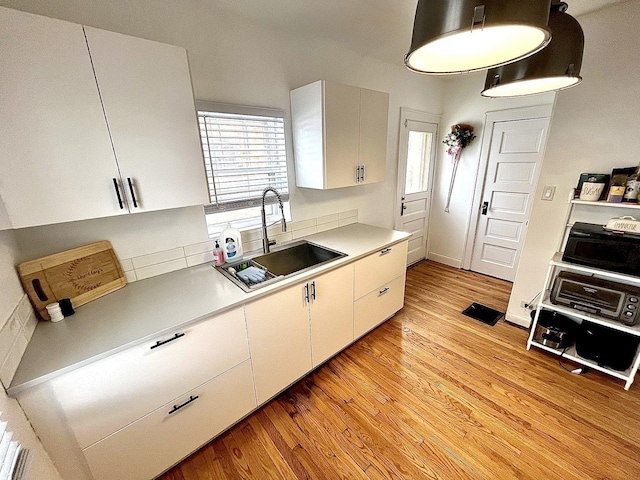 kitchen featuring white cabinets, light countertops, a sink, and light wood finished floors