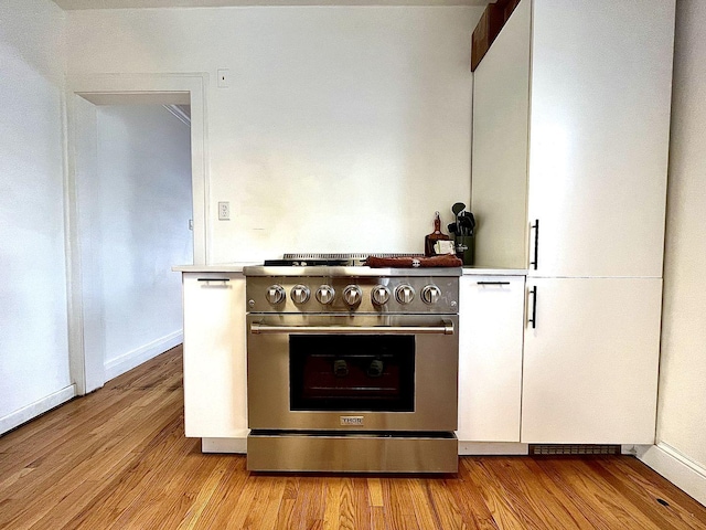 kitchen featuring high end stove, light wood-style floors, white cabinets, and light countertops