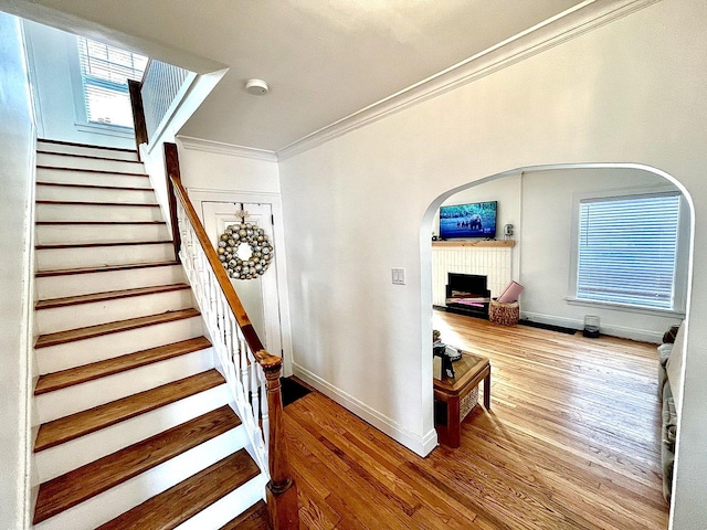 stairway featuring a fireplace with raised hearth, arched walkways, wood finished floors, baseboards, and crown molding