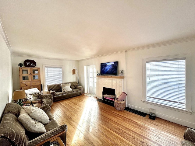 living area featuring a tile fireplace, crown molding, baseboards, and wood finished floors