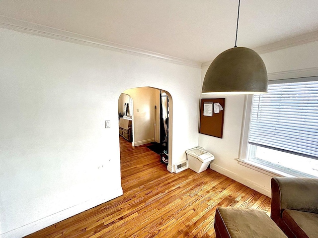 spare room featuring arched walkways, visible vents, light wood-style flooring, ornamental molding, and baseboards