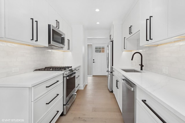 kitchen featuring a sink, white cabinetry, appliances with stainless steel finishes, light wood-type flooring, and light stone countertops