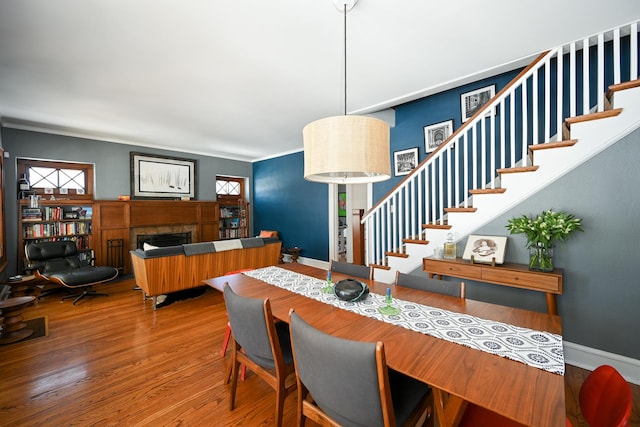 dining space with a tile fireplace, stairway, baseboards, and wood finished floors