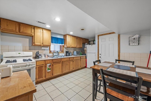 kitchen featuring light tile patterned flooring, white appliances, a sink, visible vents, and light countertops