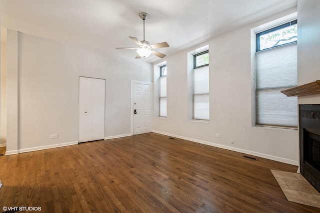 unfurnished living room with a fireplace with flush hearth, visible vents, a ceiling fan, baseboards, and dark wood-style floors