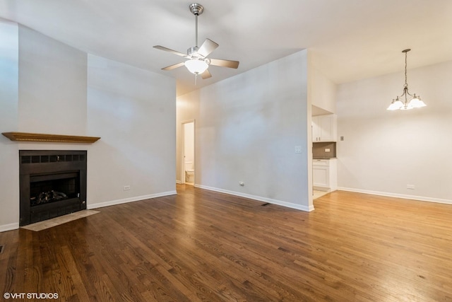 unfurnished living room with a fireplace with flush hearth, baseboards, wood finished floors, and ceiling fan with notable chandelier