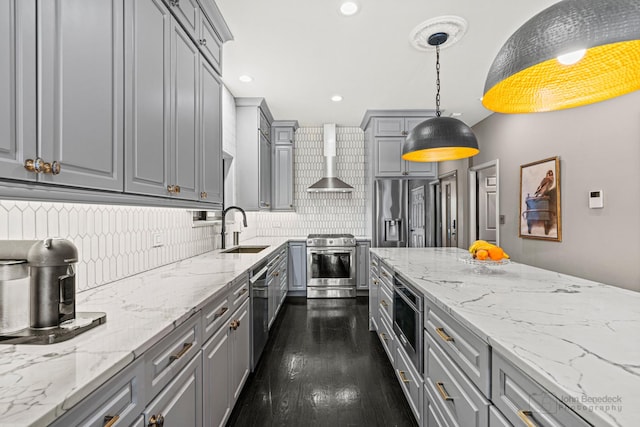 kitchen featuring wall chimney exhaust hood, decorative light fixtures, gray cabinets, stainless steel appliances, and a sink