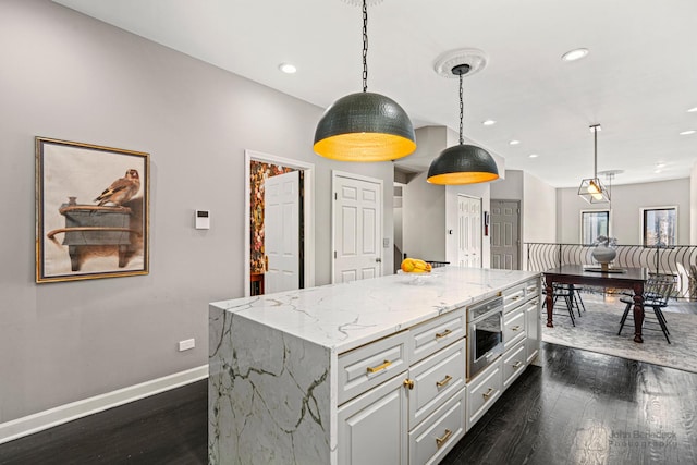 kitchen featuring pendant lighting, light stone counters, baseboards, and a center island