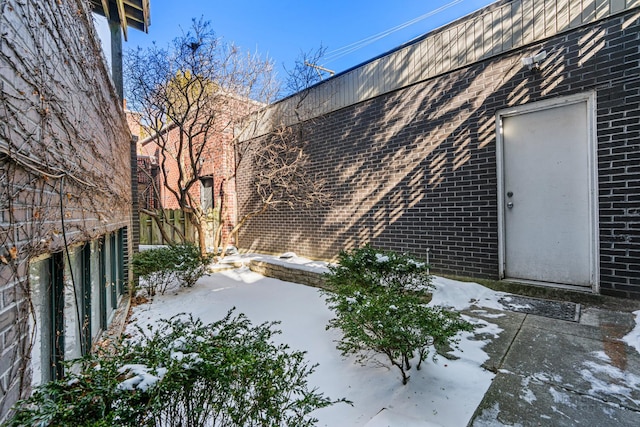 view of snowy exterior featuring fence, a patio, and brick siding