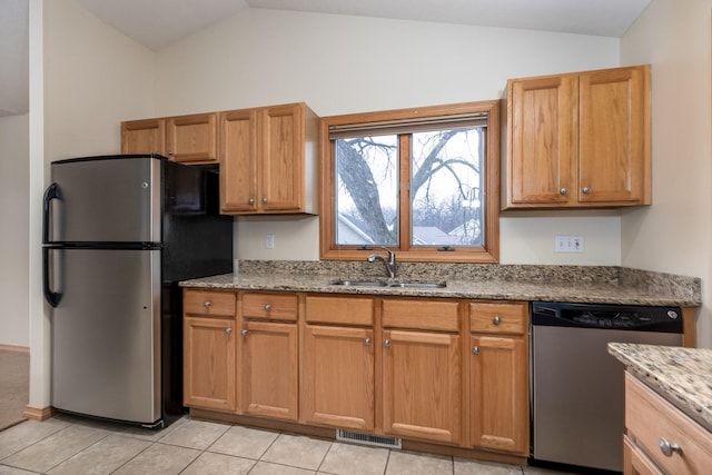 kitchen with vaulted ceiling, appliances with stainless steel finishes, a sink, and light stone counters