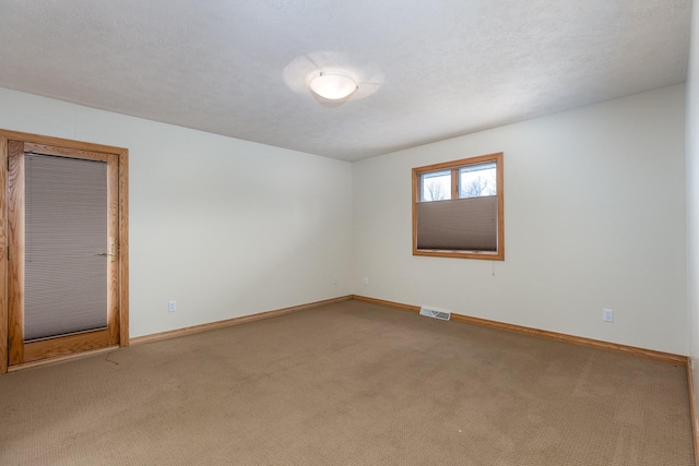 spare room featuring a textured ceiling, carpet, visible vents, and baseboards