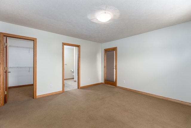 unfurnished bedroom featuring a walk in closet, a closet, light carpet, a textured ceiling, and baseboards