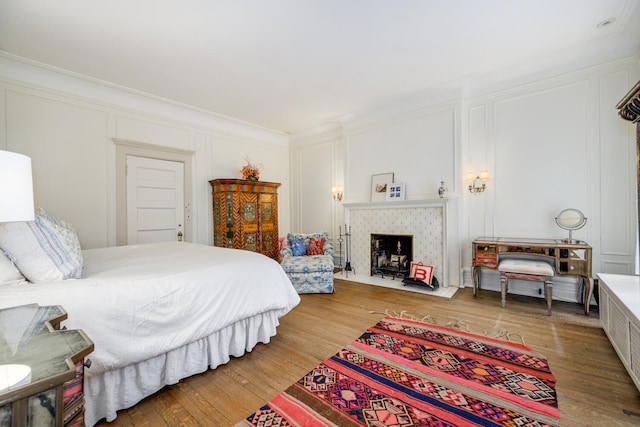 bedroom featuring a fireplace with flush hearth, ornamental molding, a decorative wall, and wood finished floors