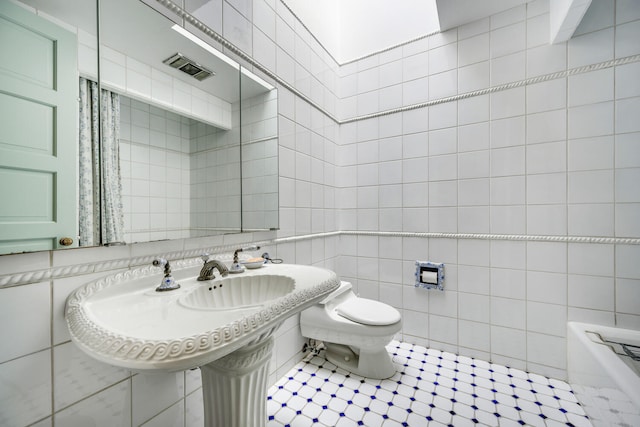 full bathroom with a tub, visible vents, tile walls, and toilet