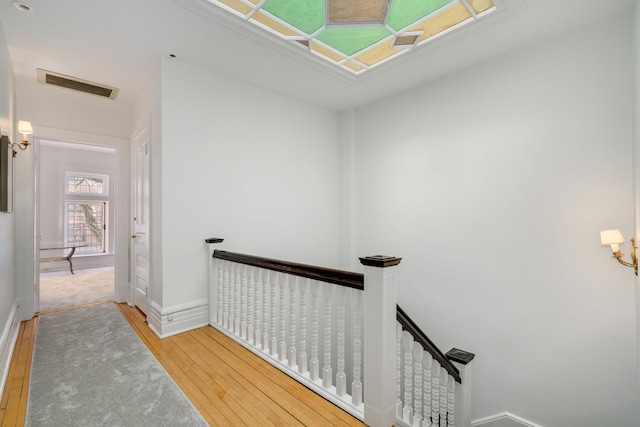 hallway with visible vents, wood finished floors, an upstairs landing, and baseboards