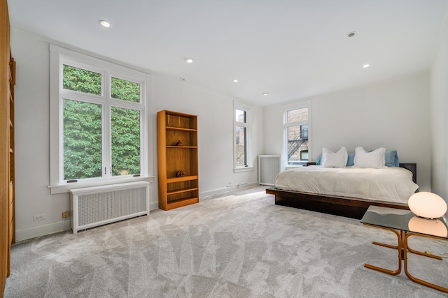 bedroom featuring radiator heating unit, multiple windows, baseboards, and light colored carpet