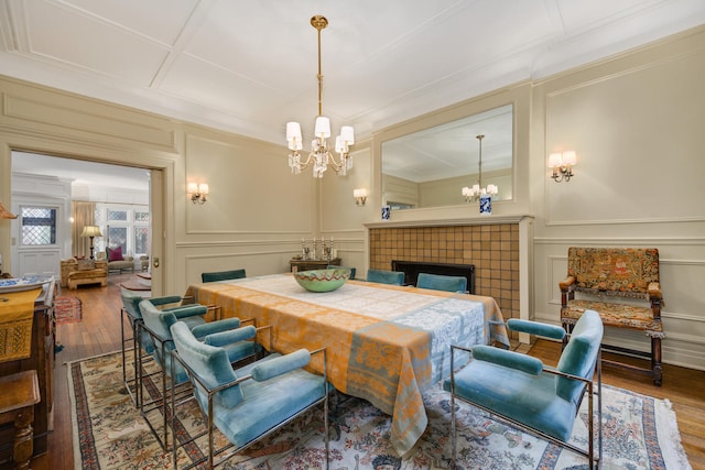 dining space featuring a tile fireplace, an inviting chandelier, wood finished floors, and a decorative wall