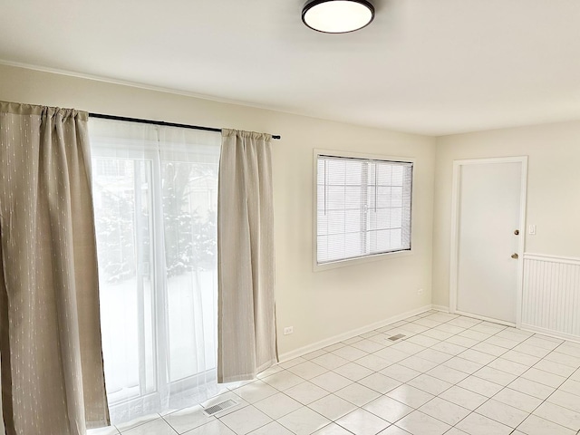 spare room featuring wainscoting, visible vents, baseboards, and light tile patterned floors