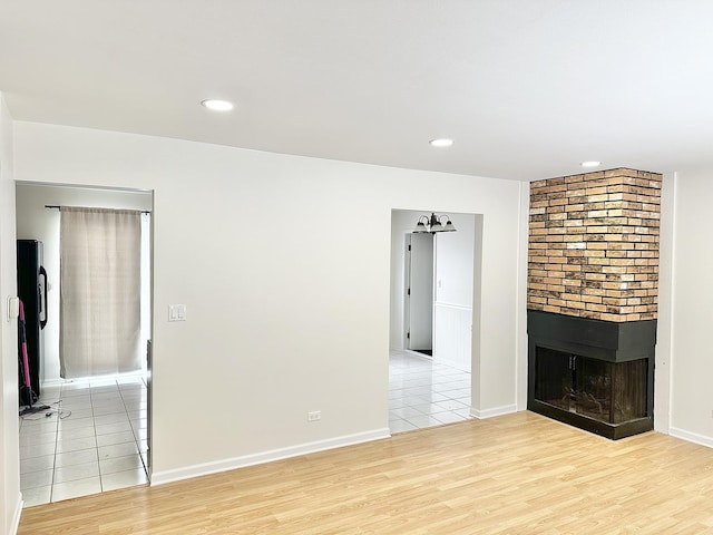 unfurnished living room with light wood finished floors, a fireplace, recessed lighting, and baseboards