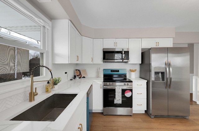 kitchen featuring a sink, white cabinetry, decorative backsplash, light stone countertops, and appliances with stainless steel finishes