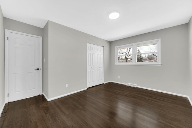 unfurnished bedroom featuring dark wood-type flooring, a closet, visible vents, and baseboards