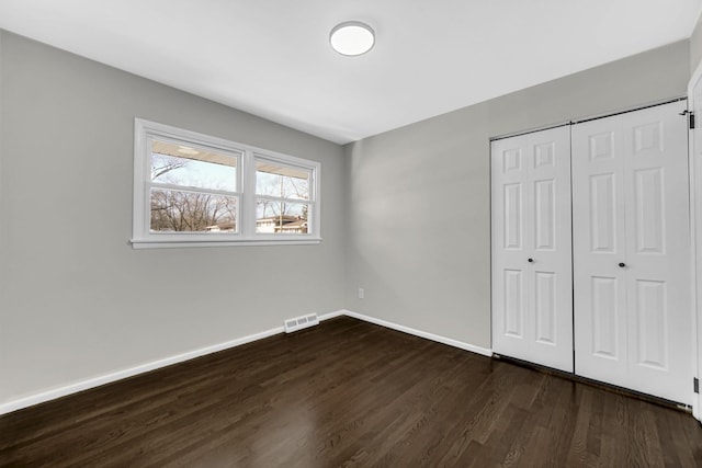 unfurnished bedroom with dark wood finished floors, baseboards, visible vents, and a closet