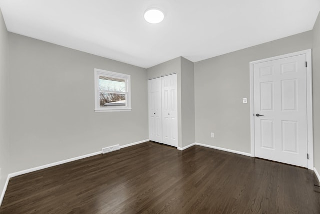 unfurnished bedroom with a closet, visible vents, baseboards, and dark wood-style flooring