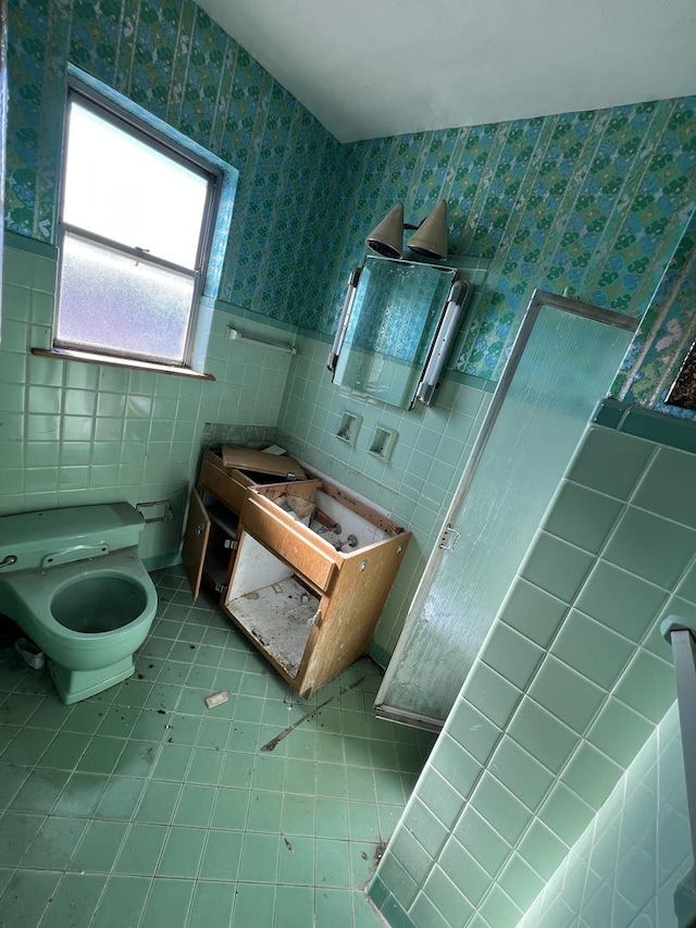 bathroom with toilet, wallpapered walls, tile walls, and wainscoting