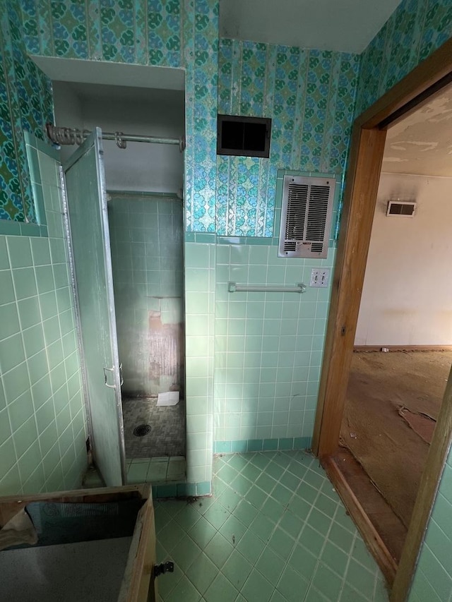 bathroom with wallpapered walls, wainscoting, tile patterned flooring, a shower stall, and tile walls