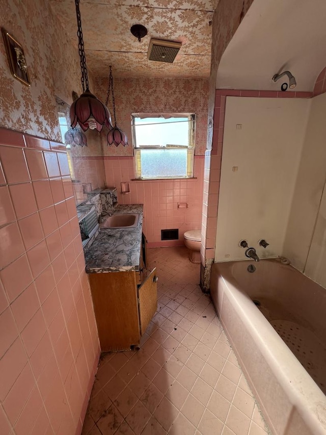 bathroom featuring toilet, visible vents, vanity, tile walls, and washtub / shower combination