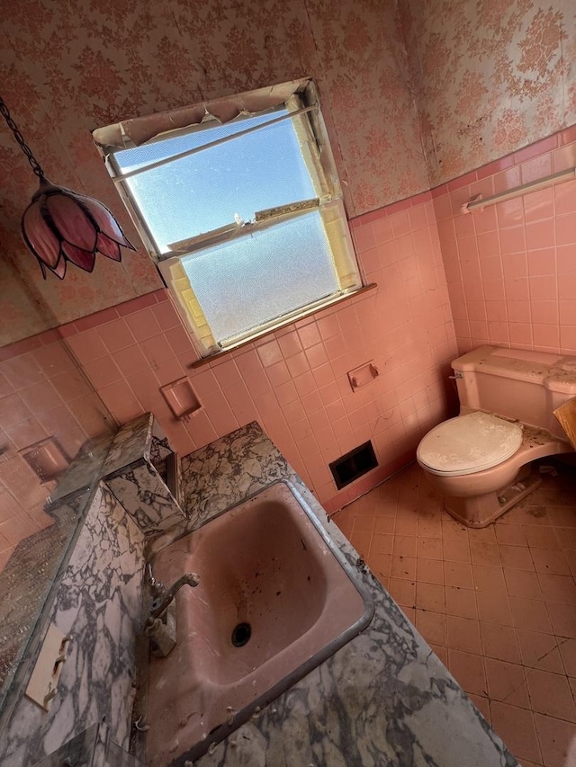 bathroom with a wainscoted wall, tile walls, toilet, and wallpapered walls