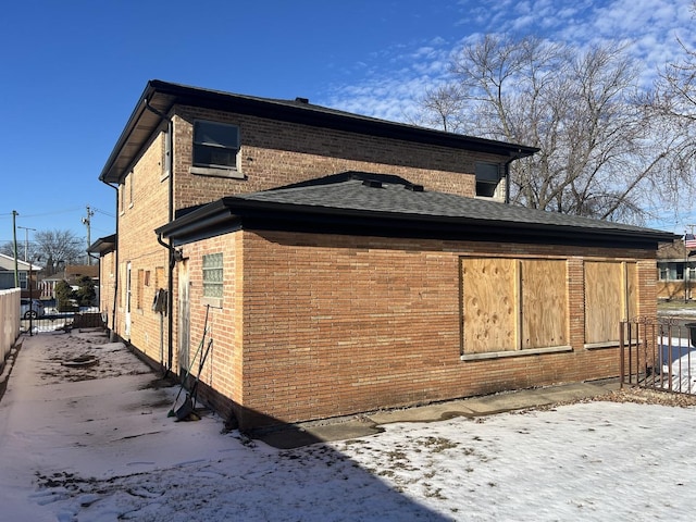 view of snowy exterior featuring brick siding and fence