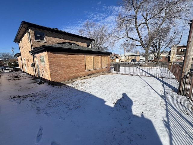 view of snow covered exterior featuring brick siding, fence, and a residential view